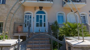 A multi-story building with a central entrance featuring a metal archway and a staircase leading to the ground floor. - Apartments Seper (Crikvenica)