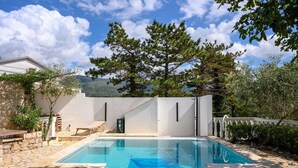A swimming pool with stone tiles, a white building, and surrounding greenery. - Apartments Seper (Crikvenica)