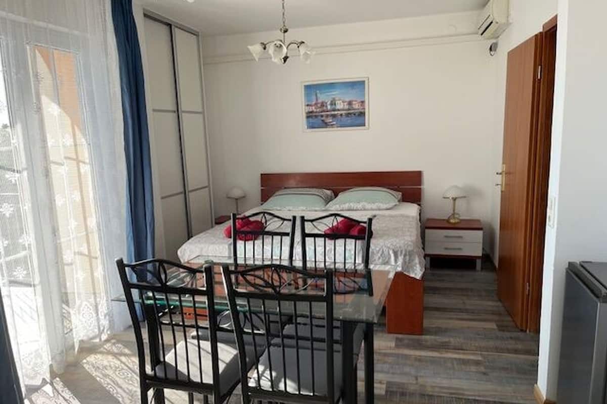 Ein Schlafzimmer mit Bett, Schreibtisch, Stuhl, einem Fenster mit Vorhängen und einem Bild an der Wand.