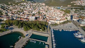 An aerial view of a coastal town with a marina, dense residential area, and mountains in the background. - Apartments Seper (Crikvenica)
