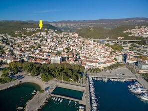 Ett flygbildsbild av en kuststad med tättbebyggda områden, en småbåtshamn med båtar och en tydlig gul pil som pekar mot en specifik plats.