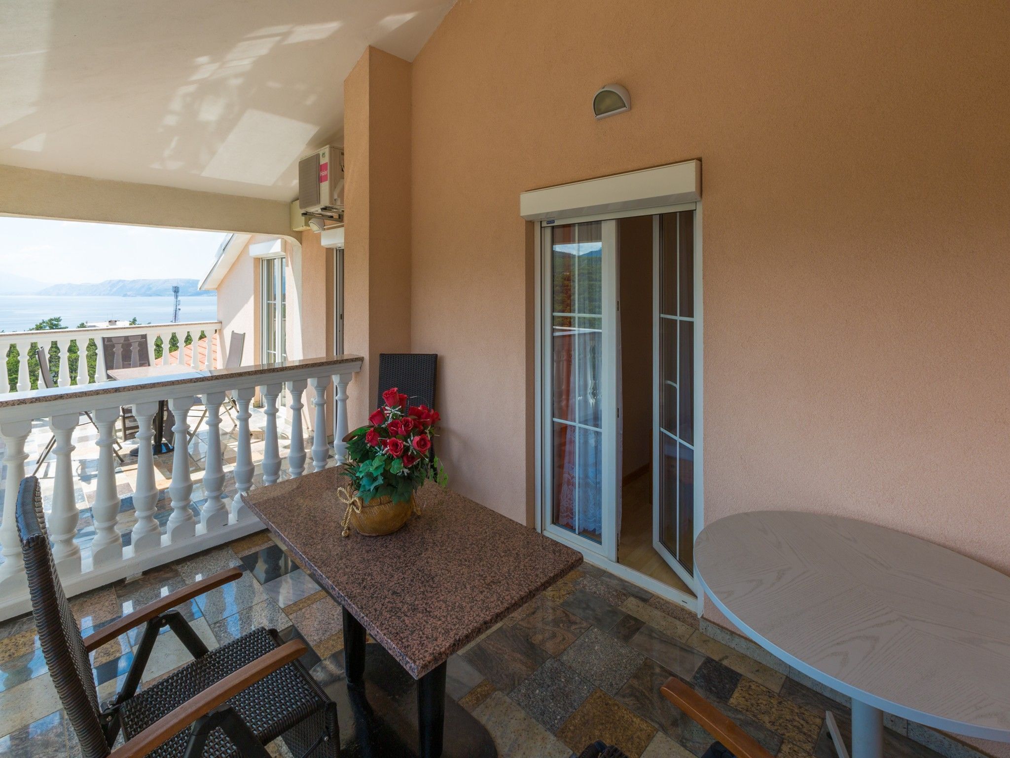 Ein Balkon mit Tisch und Stühlen, einem Blumentopf und Blick auf das Meer.
