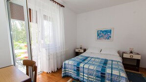 Une chambre à coucher comprenant un lit, deux tables de chevet, une chaise, un bureau et une fenêtre avec des rideaux.