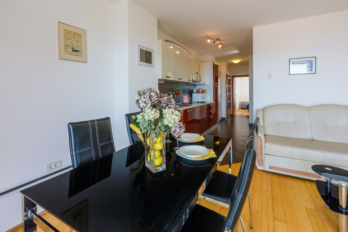 A modern living room with a black dining table, white sofa, and a kitchen in the background.