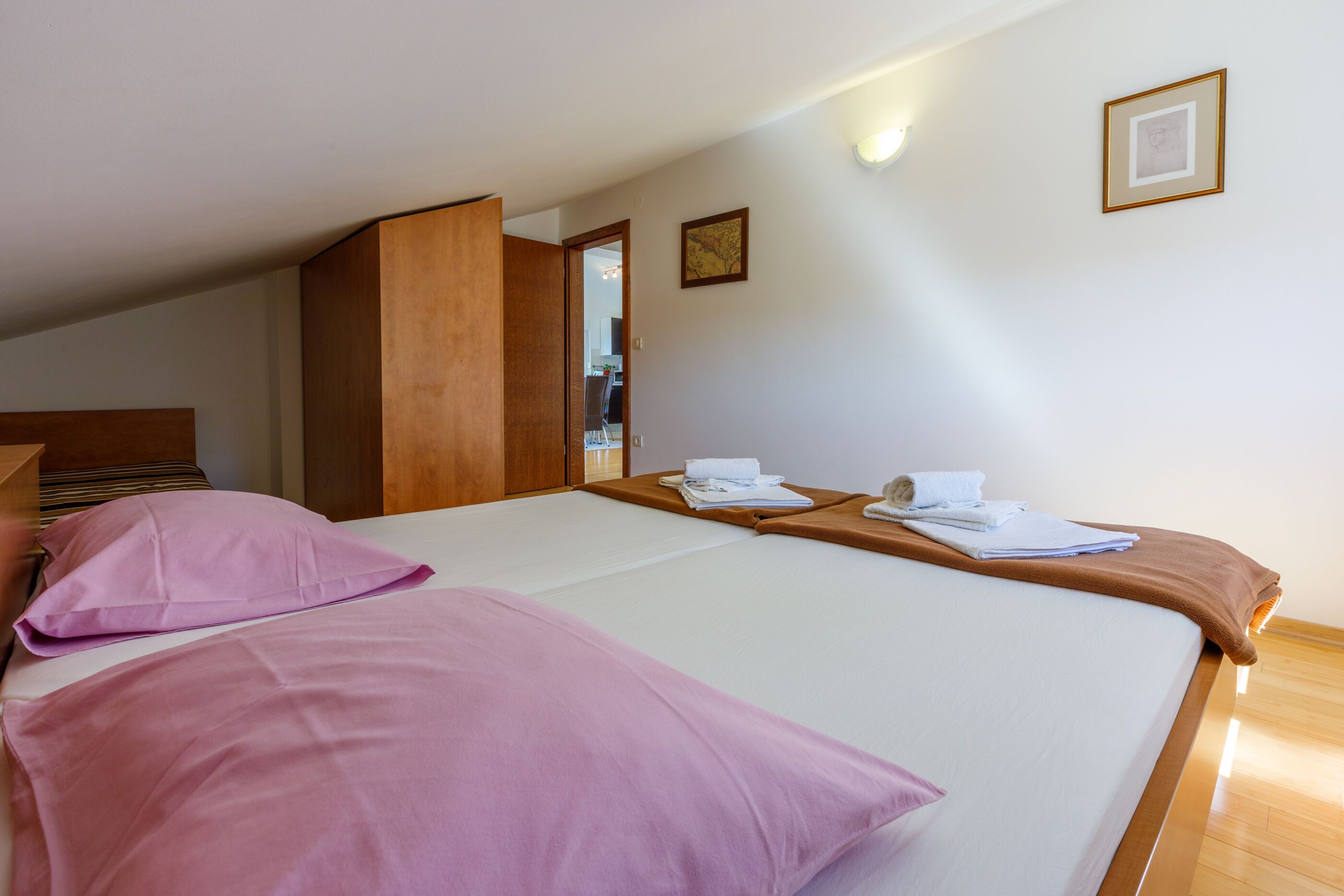 Une chambre d’hôtel avec deux lits, des têtes de lit en bois, un plancher en bois et une porte donnant sur une autre chambre.