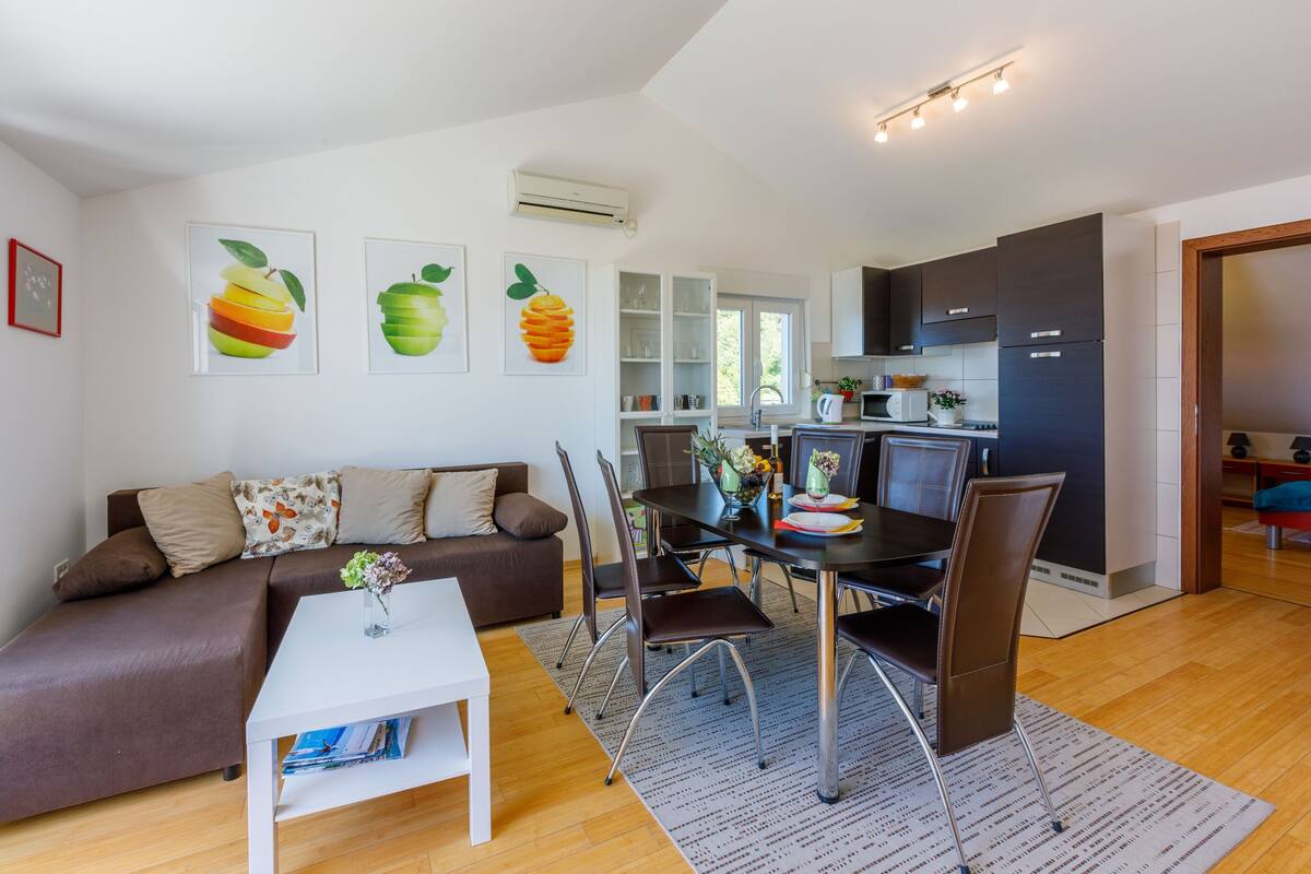 A modern living room with a brown sofa, white coffee table, and a dining area with a black table and chairs.