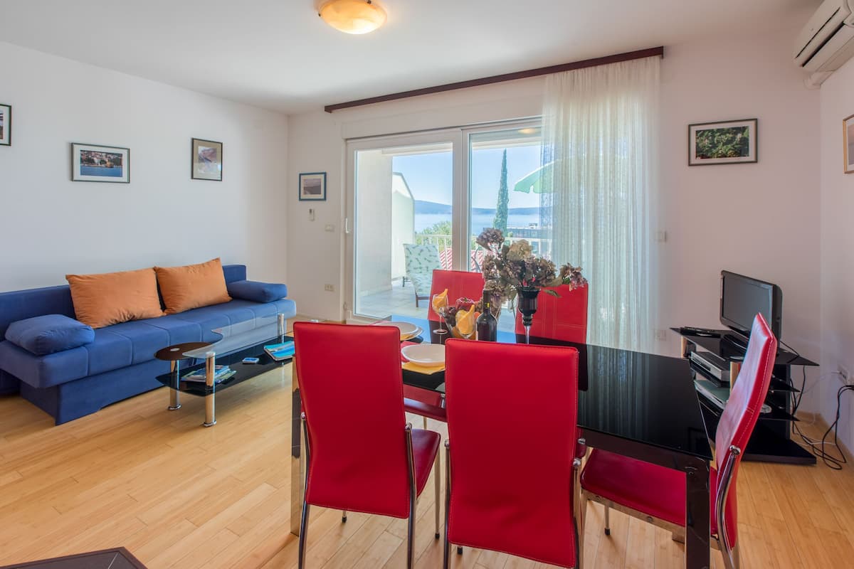 A living room with a blue sofa, red chairs, a dining table, and a TV.