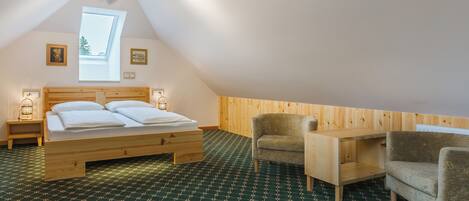 A bedroom with a sloped ceiling, a bed with white linens, a wooden desk, two chairs, and a patterned floor.