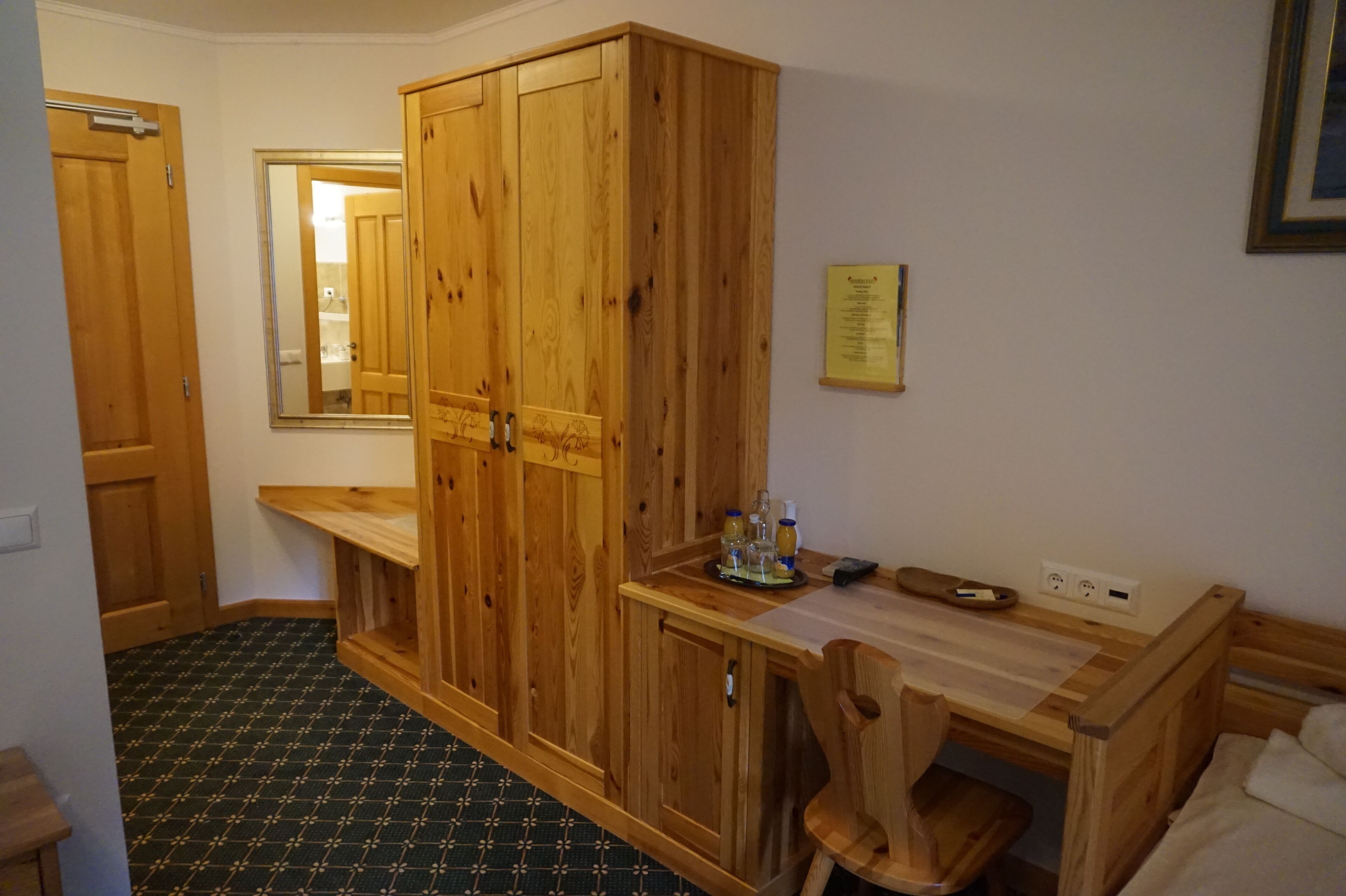 A room with wooden furniture, a mirror, a small table with bottles, and a power outlet.