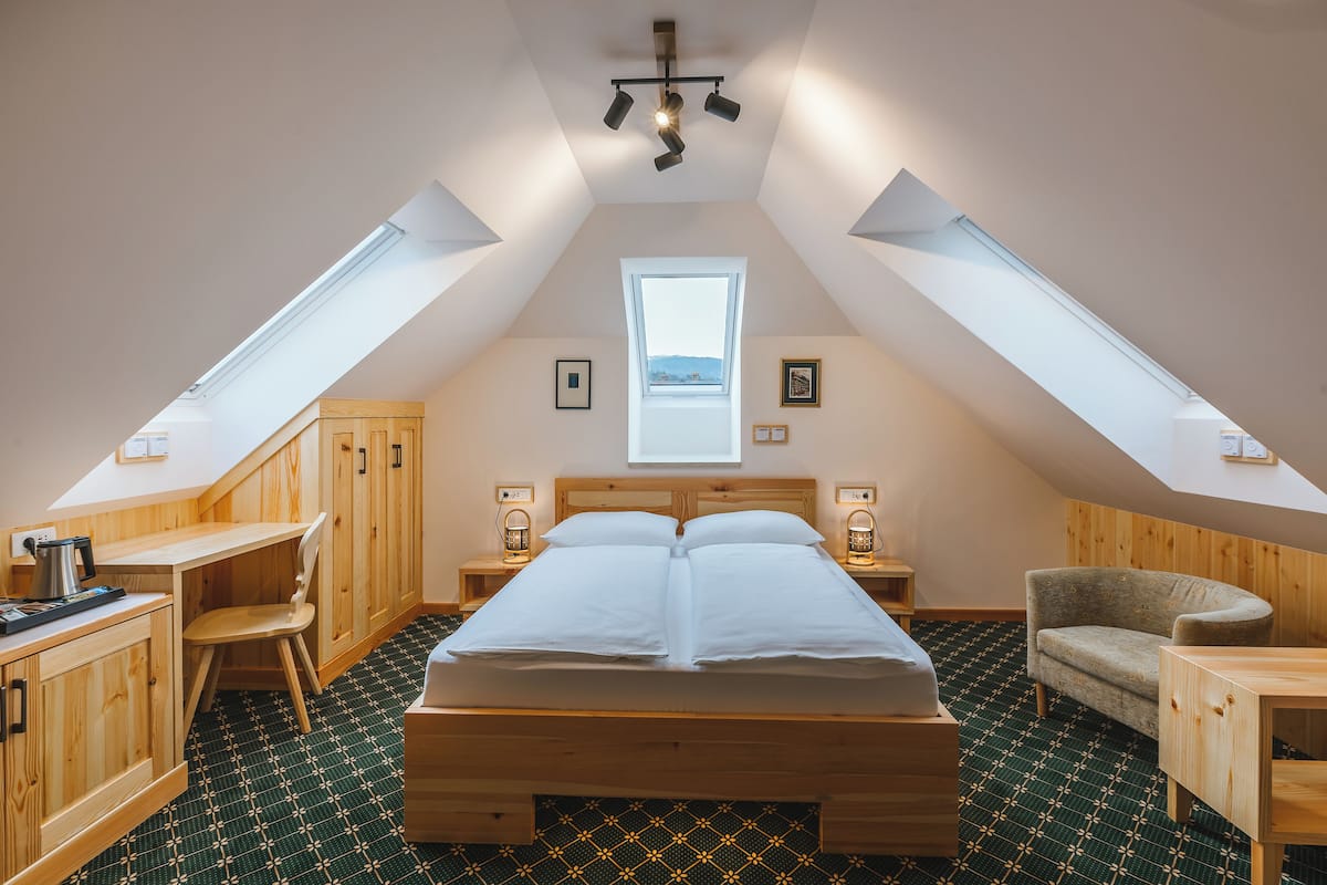 Un dormitorio con techo inclinado, tragaluces, muebles de madera, una cama y vistas a través del ventanal.