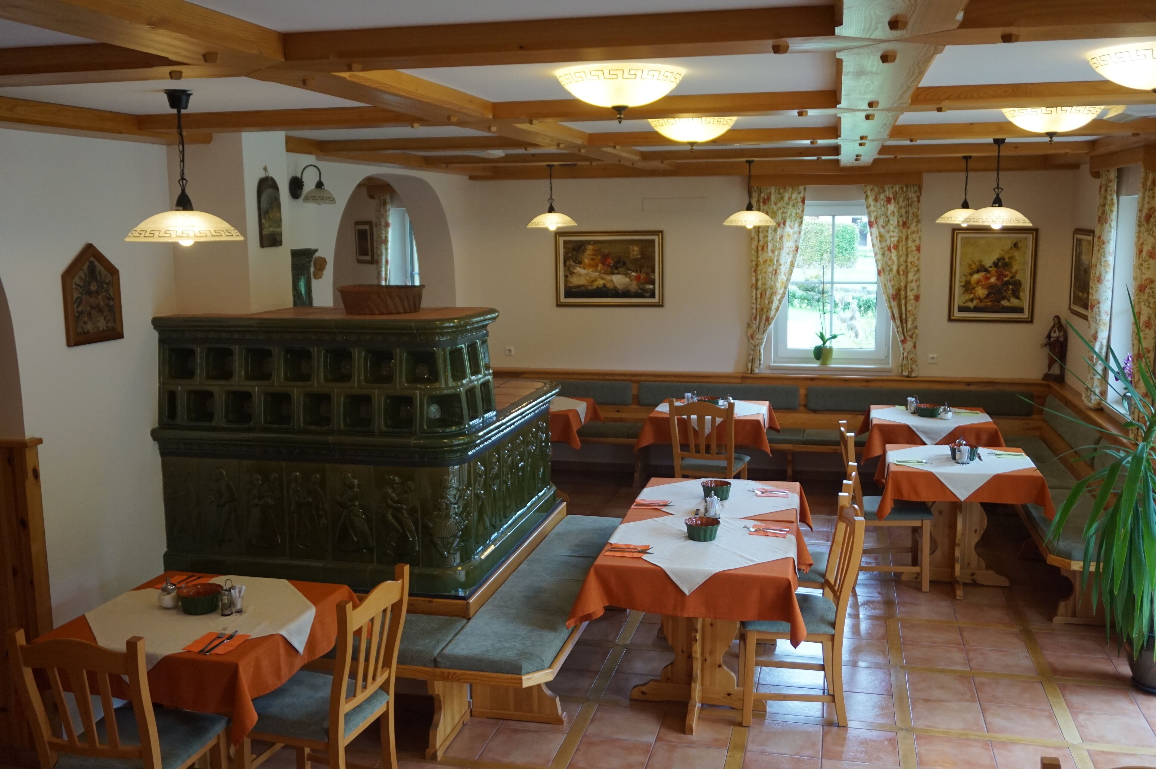 A dining area with wooden tables and benches, a central green carved structure, and hanging pendant lights.
