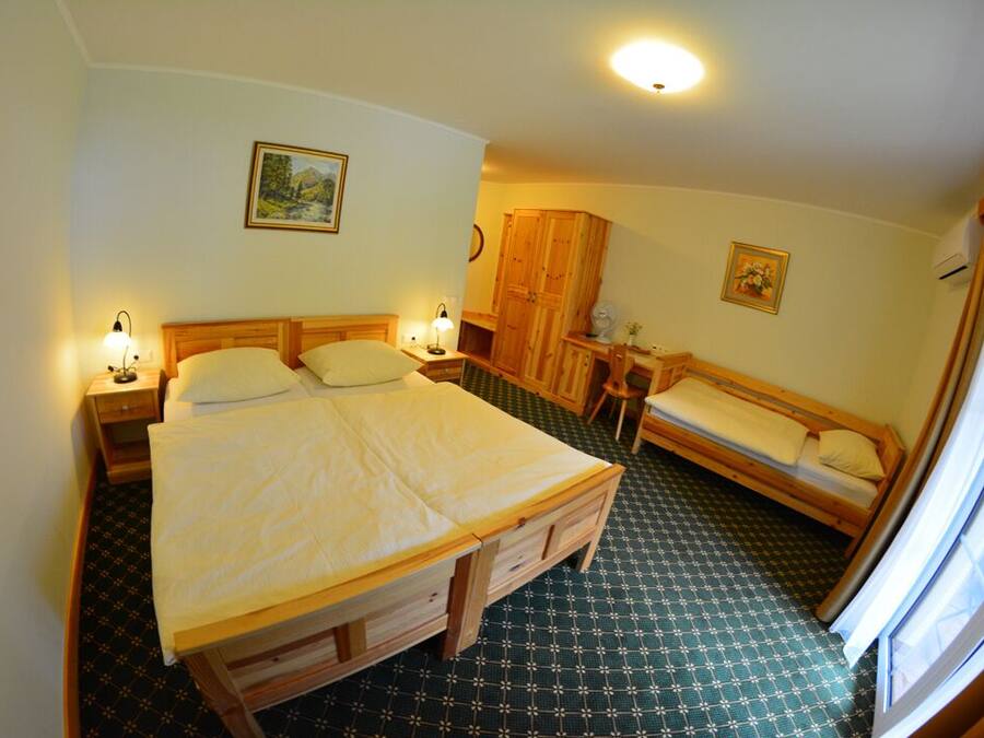 A room with a large bed, a smaller bed, a wooden wardrobe, a small table, and a window.
