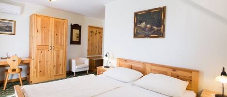 A bedroom with a large bed, wooden wardrobe, a desk with a chair, and a bedside table with a lamp.
