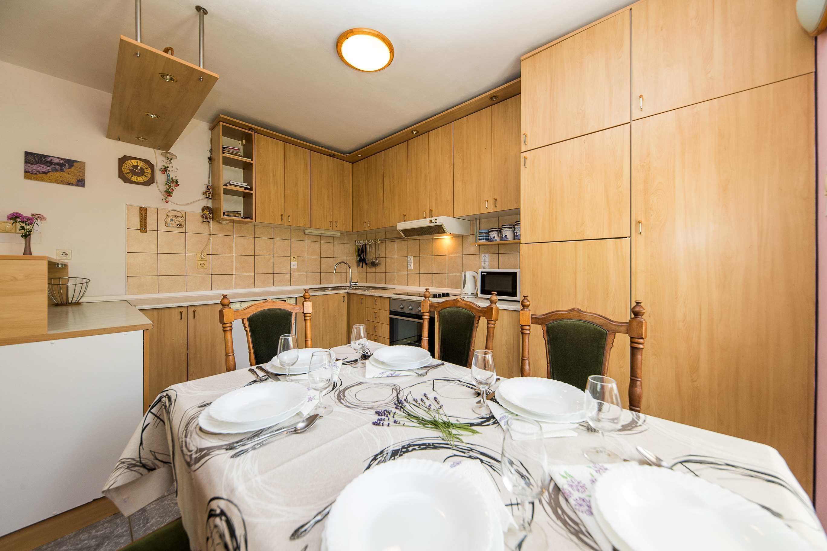 A dining area with a table set for six, wooden cabinets, a microwave, and a sink.