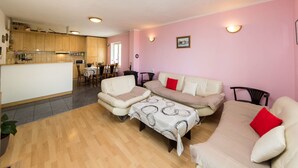 Una sala de estar con sofá, sillones y una mesa de centro. Hay una zona de cocina con armarios de madera y una mesa de comedor.