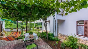 A patio with a table and chairs, surrounded by plants and a hammock. - House Marija (Labin)