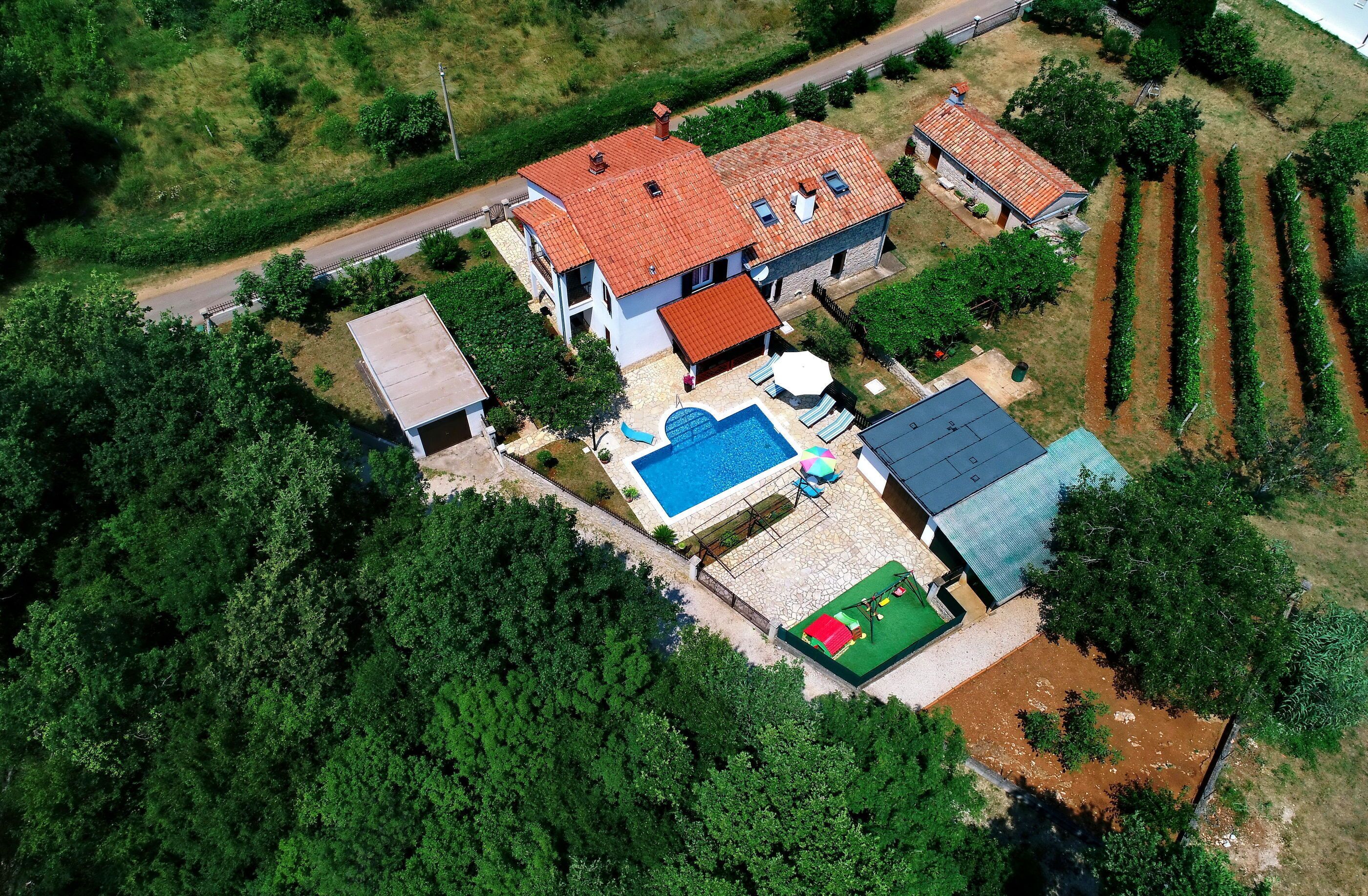 An aerial view of a two-story house with a swimming pool, a fenced garden, and a road nearby.