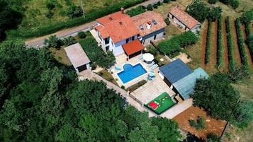 An aerial view of a two-story house with a swimming pool, a fenced garden, and a road nearby.
