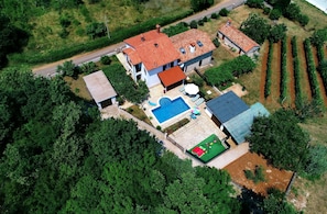 An aerial view of a two-story house with a swimming pool, a fenced garden, and a road nearby. - House Marija (Labin)