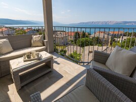 A balcony with wicker furniture, a tray with cups, and a view of the sea and buildings.