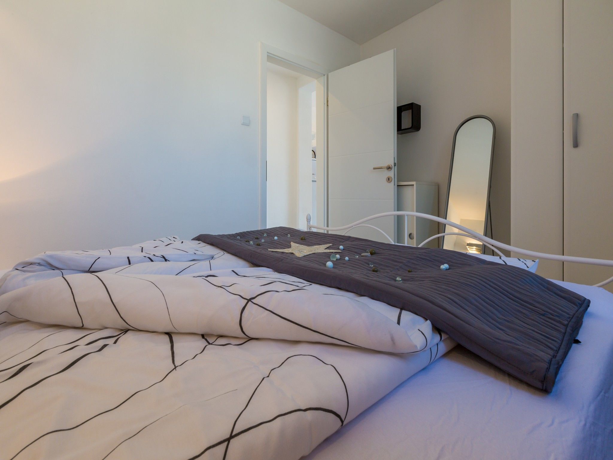 A neatly made bed with a patterned bedspread, a bedside table with a lamp, and a door leading to another room.