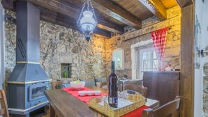 Un interior rústico con pared de piedra, estufa de leña, mesa de comedor con mantel a cuadros y una lámpara colgante.