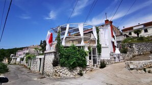 Un edificio de dos pisos con balcón, paredes de piedra y un cielo azul despejado.