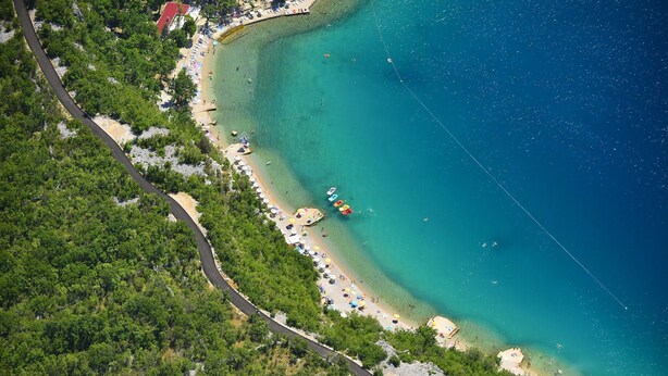 Vista aérea de una zona costera con carretera, playa y aguas azul turquesa.