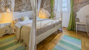 Un dormitorio con pared de piedra, cama con dosel y alfombra verde a rayas.