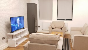 A modern living room with a television, a grey cabinet, a beige sofa, and a white brick wall. - Manhattan 5 (Maidstone)