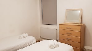 A bedroom with two single beds, a wooden dresser with a mirror, and a radiator. - Manhattan 5 (Maidstone)