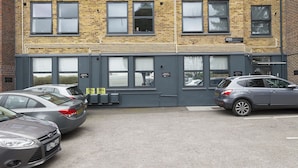 A multi-story building with a brick facade, multiple windows, and a parking area with cars. - Manhattan 5 (Maidstone)