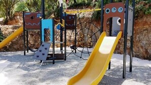A playground with a yellow slide, climbing structures, and a netted area.