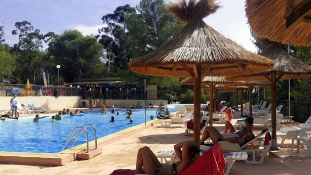A swimming pool area with lounge chairs and thatched umbrellas.