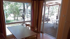 A room with a wooden table and chairs, large windows, and a sliding glass door leading to an outdoor area with chairs and a table.