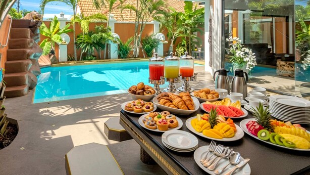 Buffet de café da manhã com frutas tropicais, doces e bebidas à beira da piscina.