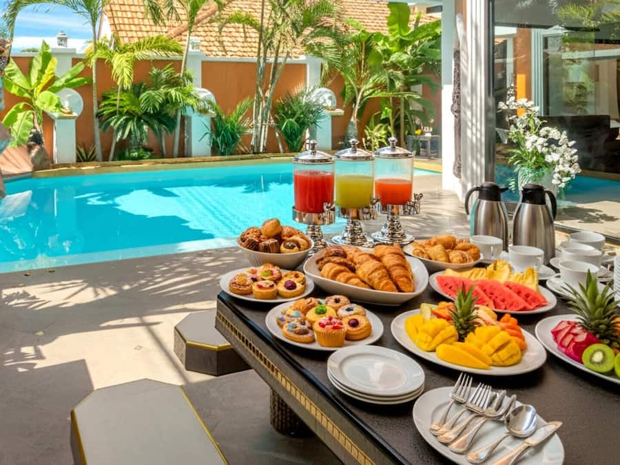 Buffet de café da manhã com frutas tropicais, doces e bebidas à beira da piscina.