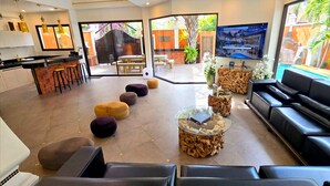 Um saguão de hotel moderno com área de refeições, disposição de assentos e uma televisão exibindo vista para a piscina.