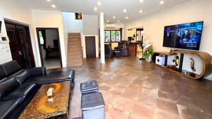 A spacious living area with a leather sofa, a coffee table, and a TV on a wooden stand.
