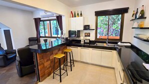 A modern kitchen with a bar area, white cabinets, and a large window with a view of greenery.