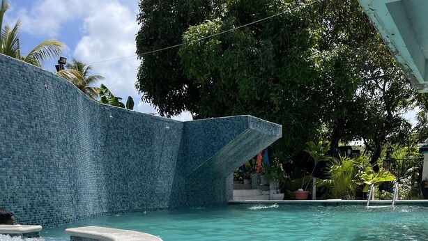 A clear blue pool with tiled edges, surrounded by lush greenery and a tiled wall. - The Hummingbird Villa Luxury Suite- Vacation Rental Beach Resort Villa in Mayaro (Guayaguayare)