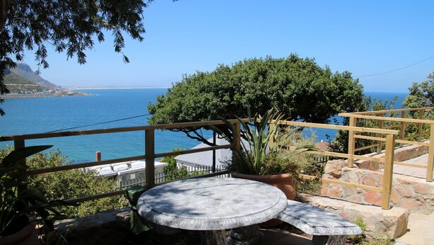 Een terras met een stenen tafel en bank, met uitzicht op de kust onder een heldere lucht.
