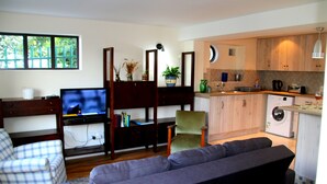 Een woonkamer met een bank, fauteuil en televisie. Er is een keuken met houten kasten en een wasmachine.