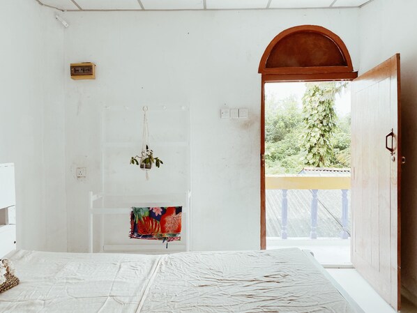 Quarto com cama, planta pendurada, tecido colorido e porta de madeira que dá para o exterior.