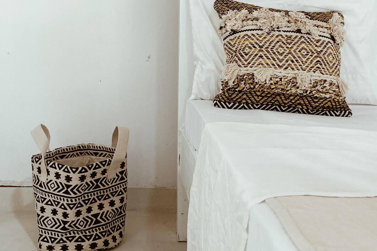 A bed with a white headboard, two patterned pillows, and a woven basket with handles.