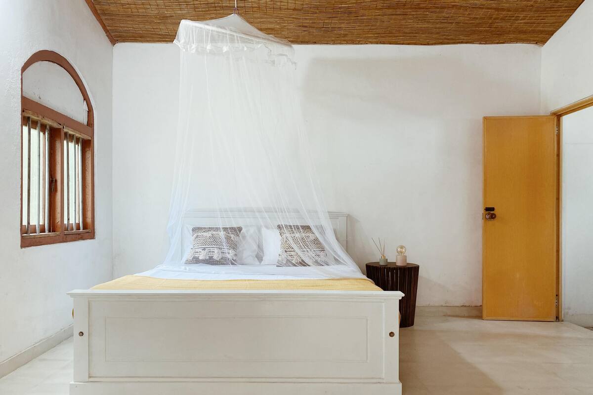 A bed with a canopy, a wooden door, and a small round table with a candle.