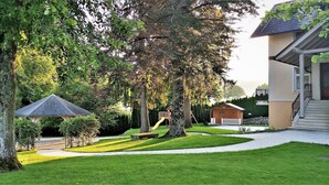A well-maintained garden with a gazebo, a playground, and a building with a porch. - Vila Ključe Apartments (Bled)