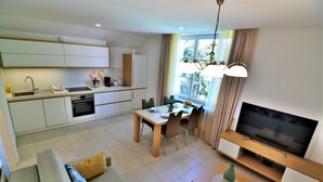 A modern living room with a sofa, dining table, chairs, a TV, and a kitchen area with cabinets and appliances. - Vila Ključe Apartments (Bled)