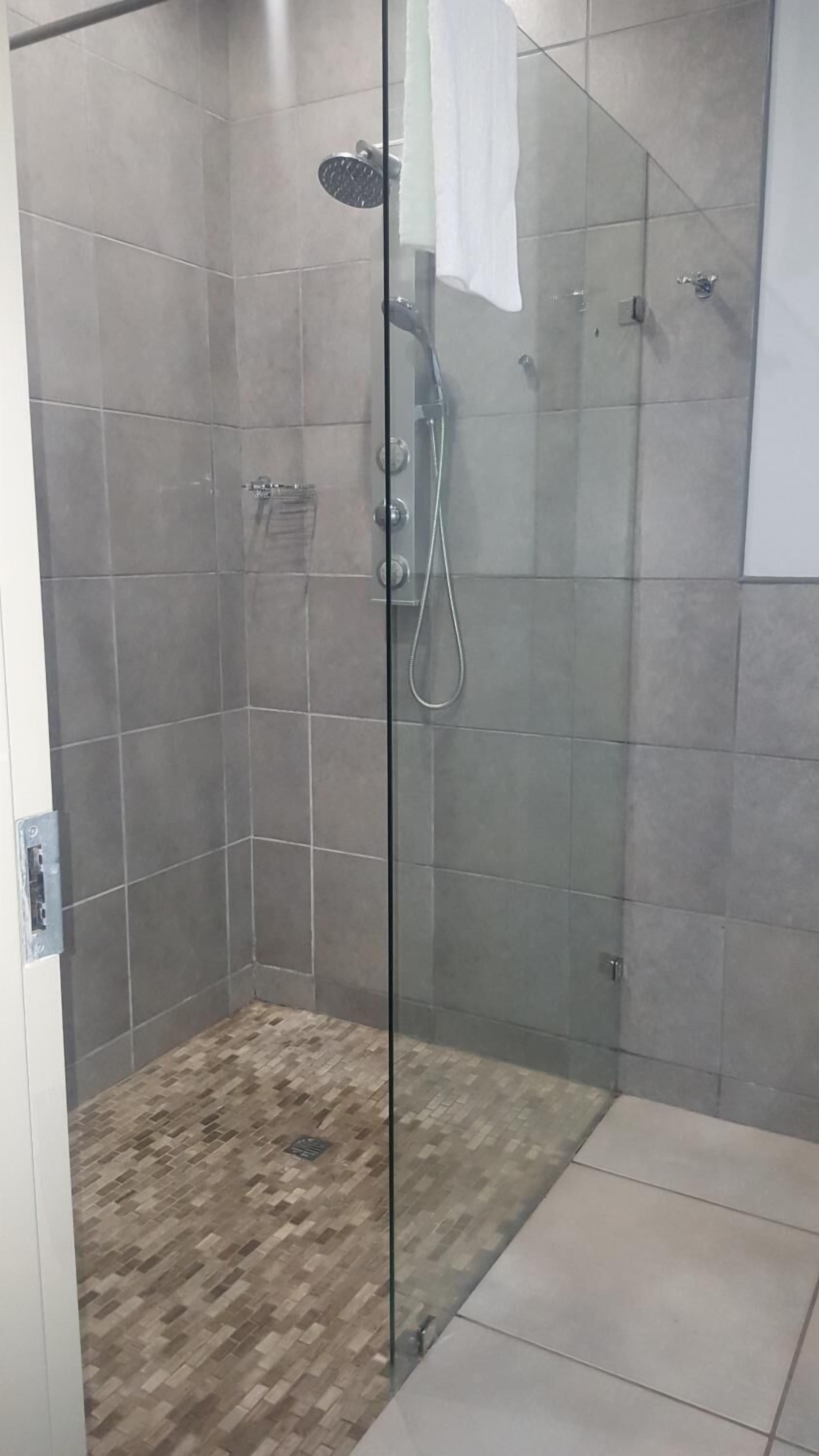 A glass-enclosed shower area with tiled walls and a wooden floor.