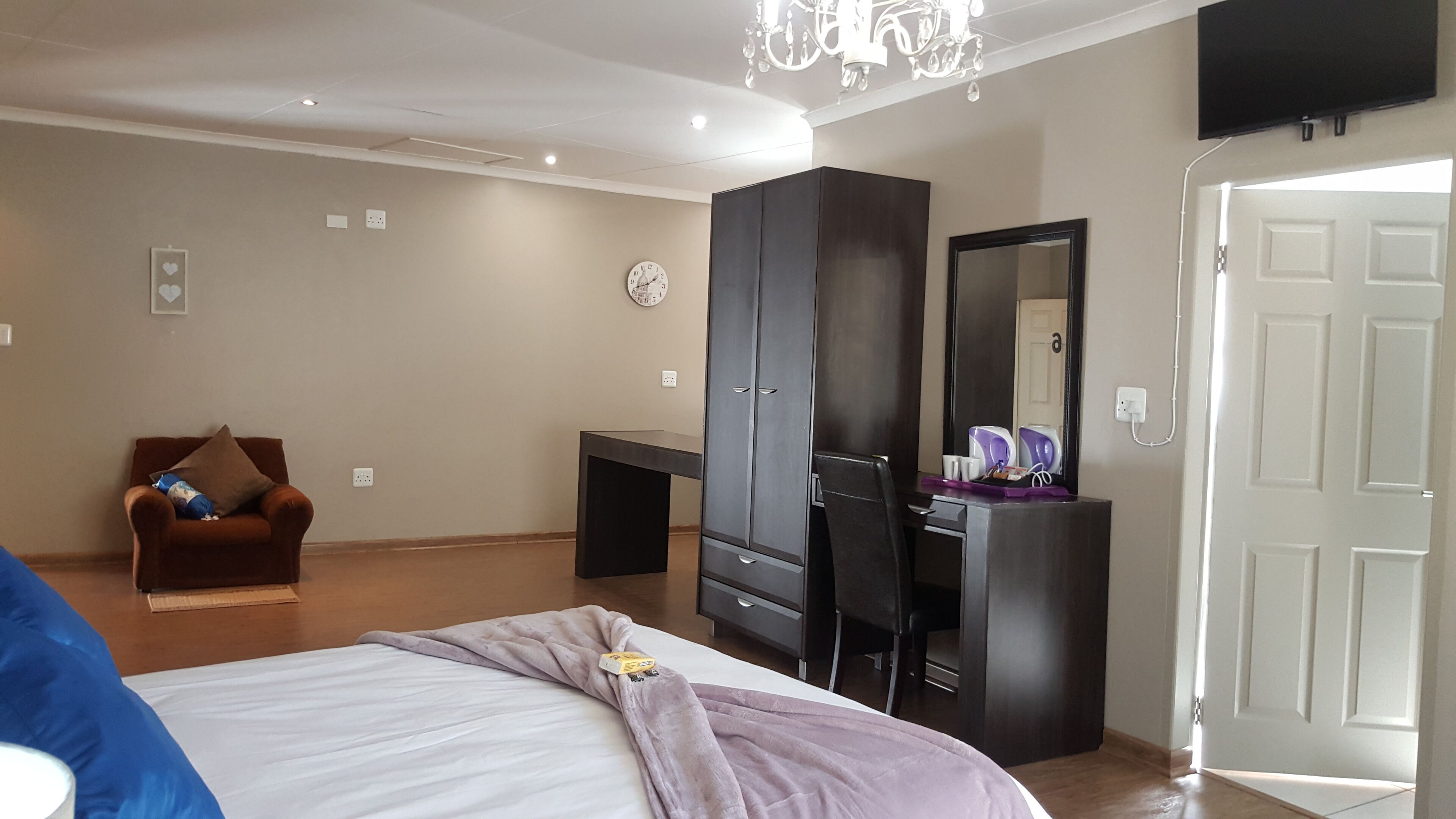 Een slaapkamer met een bed, een bureau, een kledingkast, een stoel, een klok en een televisie.